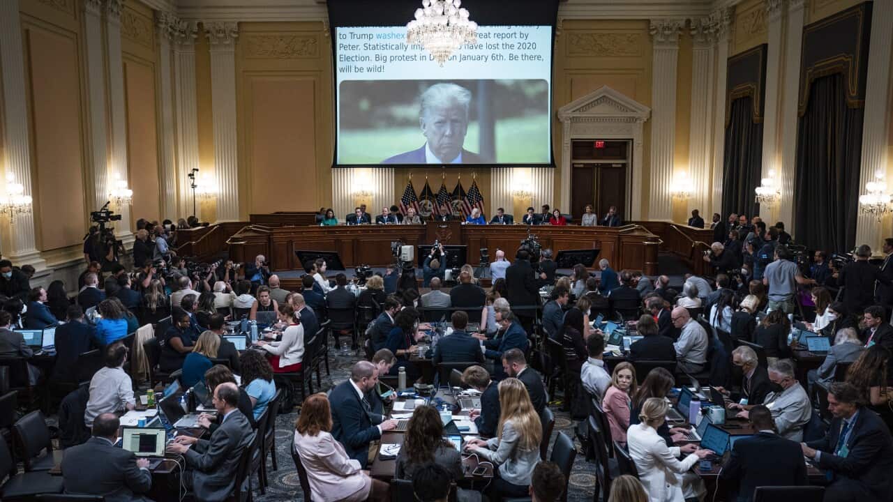 Several people watch from different areas in a room as a man's face appears on a projector.