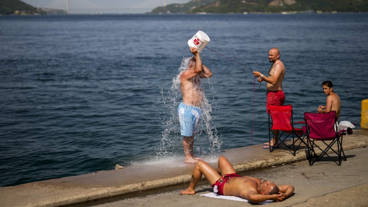 People cooling off by the water, one person throwing a bucket of water over their head.