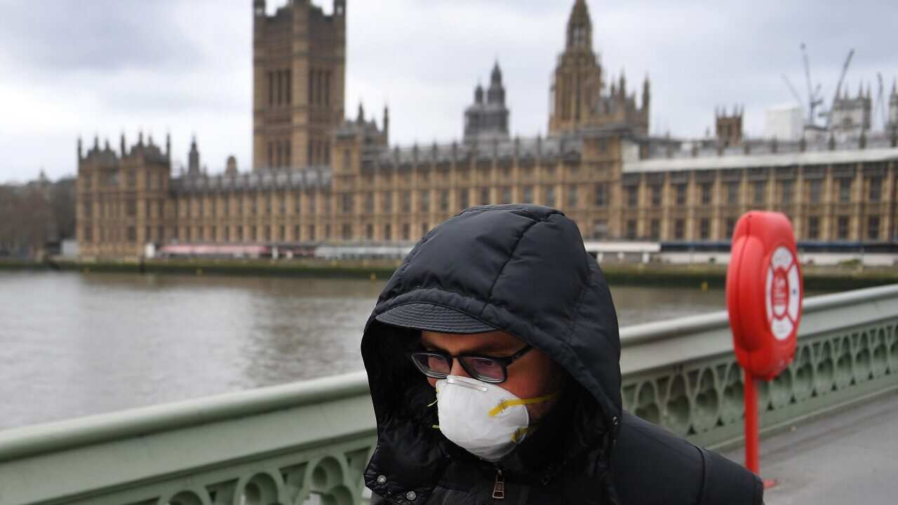 A man wearing a protective face mask walks past Westminster Palace parliament in London, Britain, 18 March 2020.