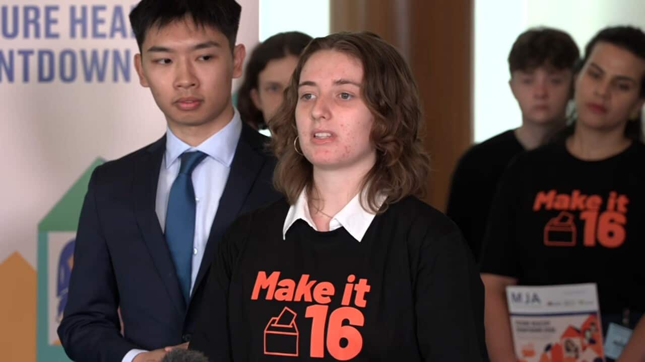 A woman in a black t-shirt, gesturing with her left hand.