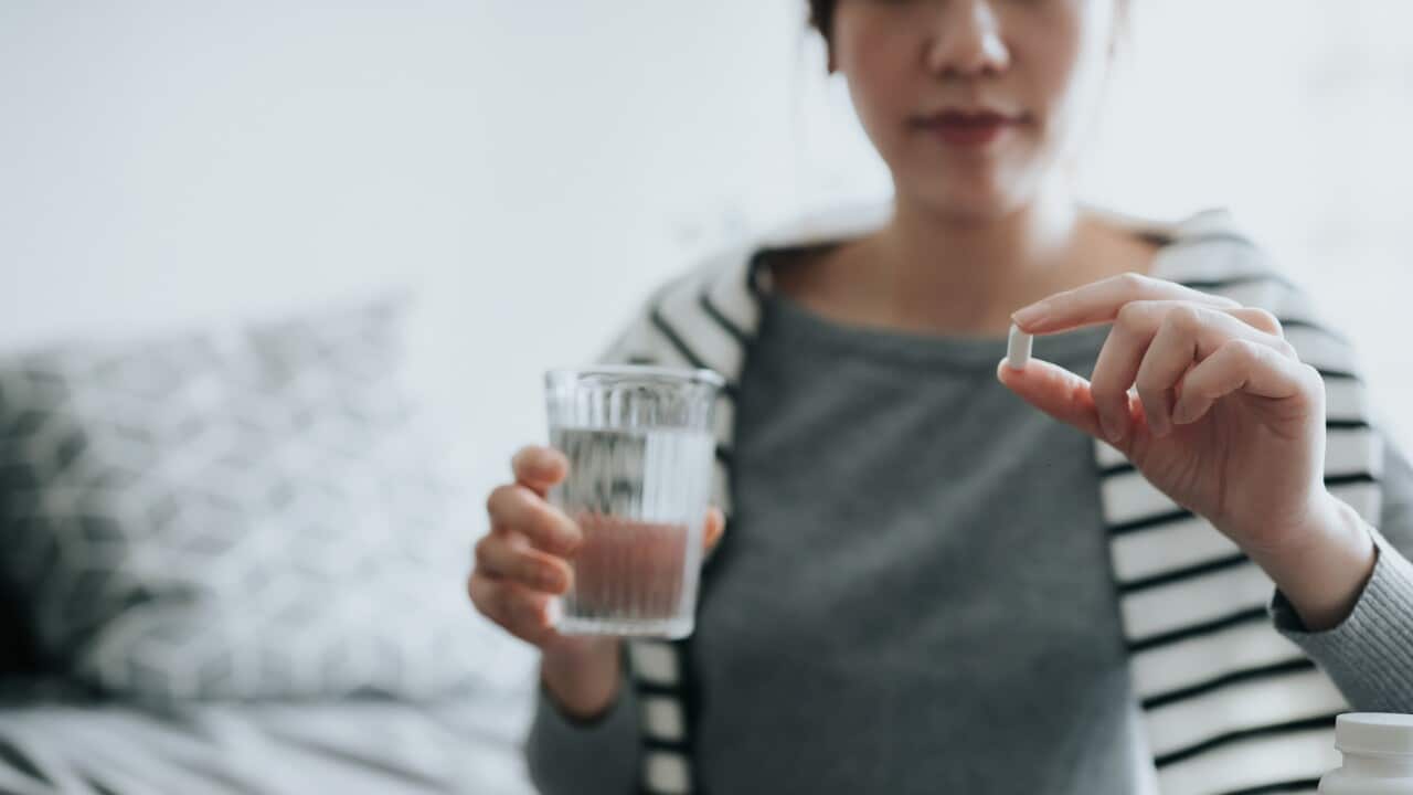Young Asian woman taking medicines with a glass of water at home, with a pill bottle by the side. Medicine, healthcare and people concept