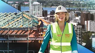 A minister in high-vis vest and a house under construction