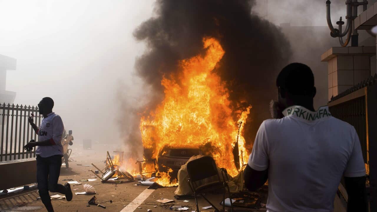 A car burns after being set alight by protesters outside the parliament building in Burkina Faso as people protest against their longtime President Blaise Compaore. (AAP)