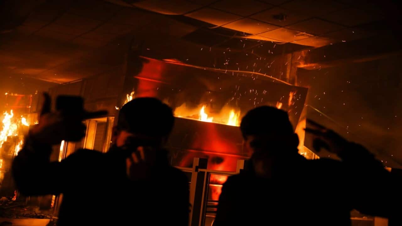 Protesters gesture as the Macul Metro station burns during a mass fare-dodging protest in Santiago, on October 19, 2019