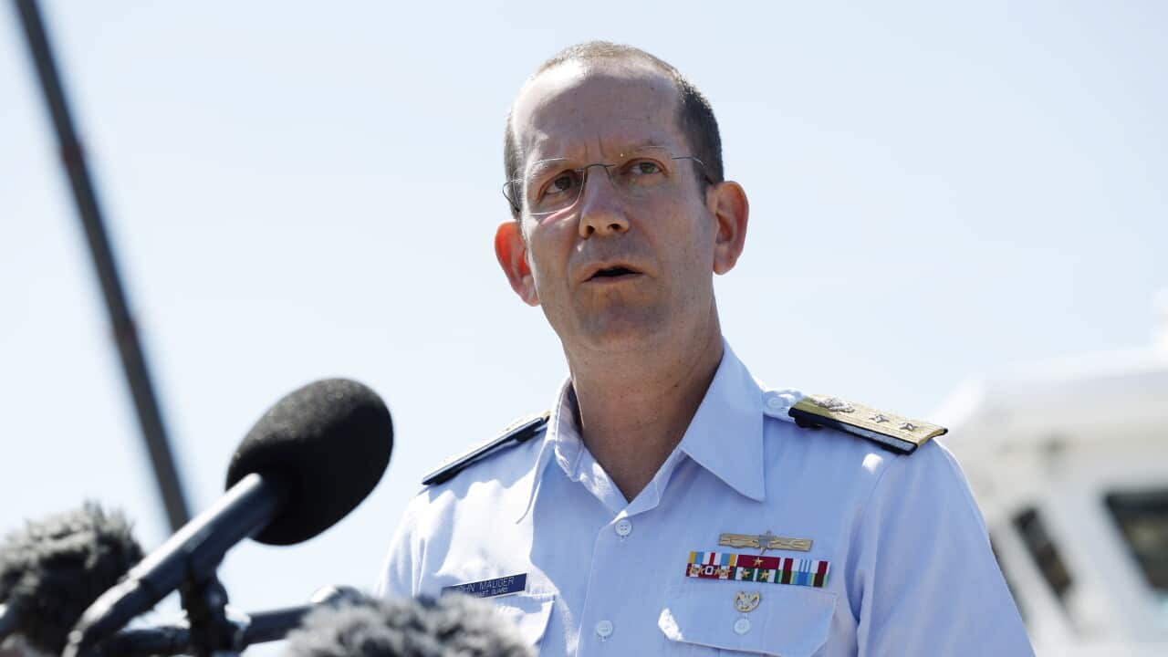 A man in a US Coast Guard uniform speaks in front of a microphone.