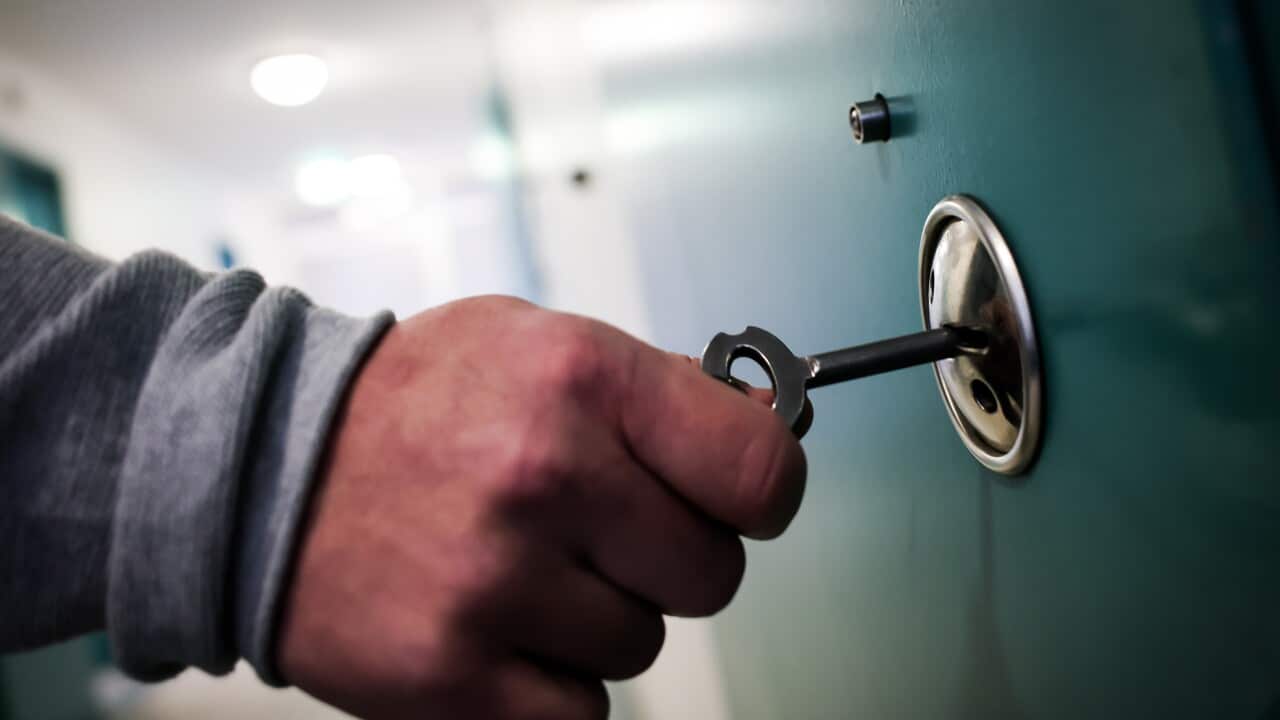 A correctional officer opens the door to a cell room