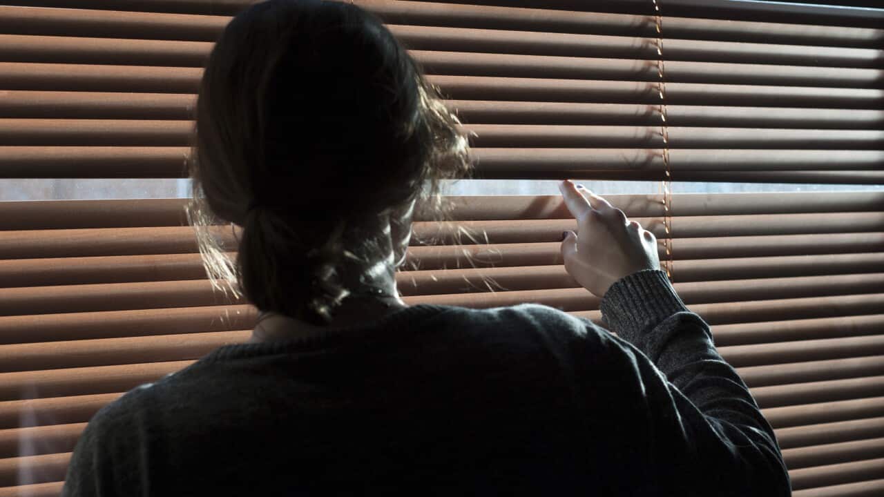 A woman looks out a window through a blind. Picture posed by model - model release available..