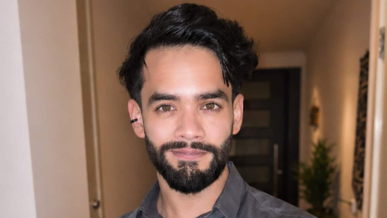 Bashshar Khalid stands indoors with his arms crossed, wearing a grey button-up shirt.