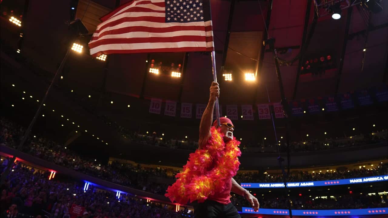 A man wearing orange carries the American flag in front of a stadium crowd.