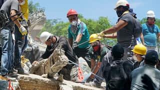 A group of people in hard hats use ropes to lift fallen logs and concrete.