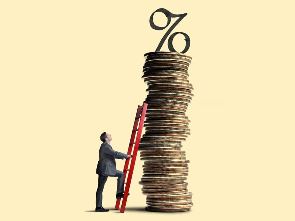 Man Leans Ladder Against Tall Stack Of Coins Topped With Interest Rate Symbol