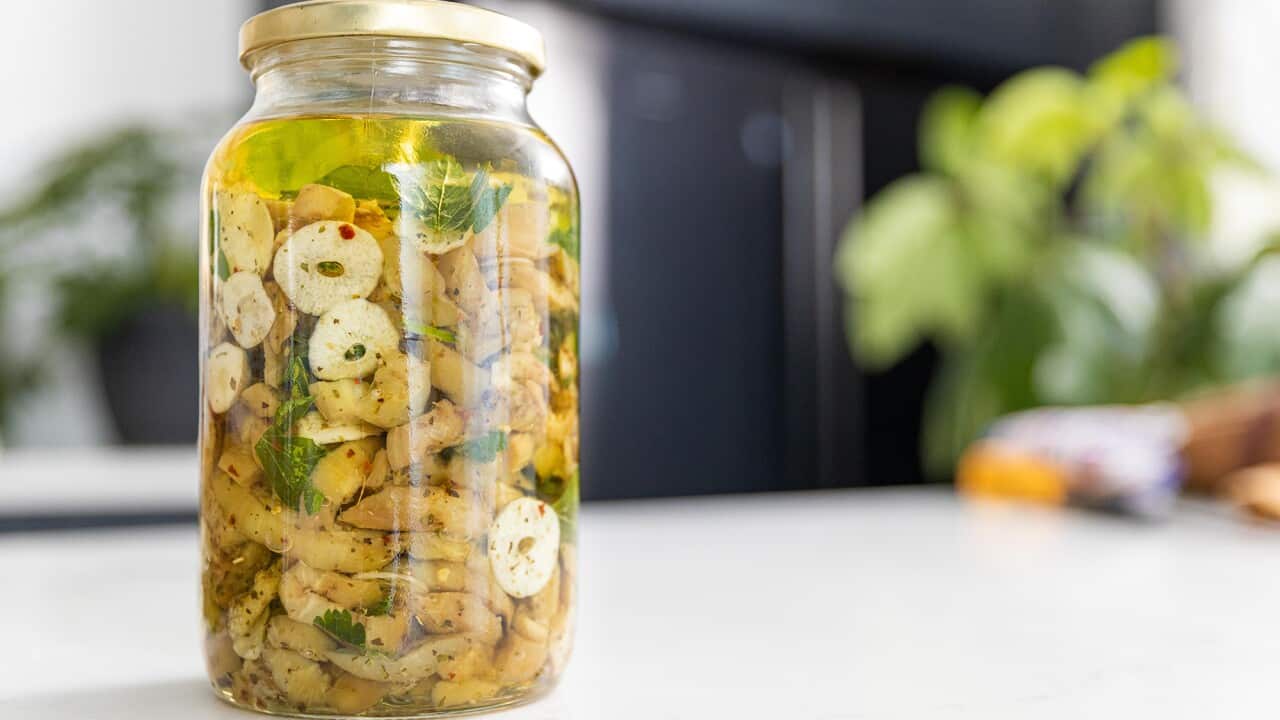 A glass jhar holds pieces of eggplant and slices of garlic in a golden liquid.