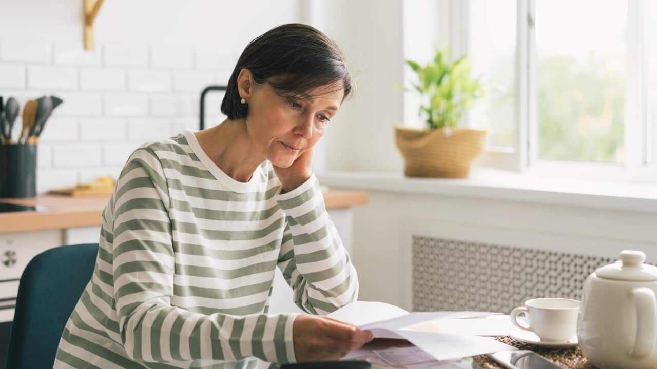 A woman looks down at a piece of paper at her kitchen table.