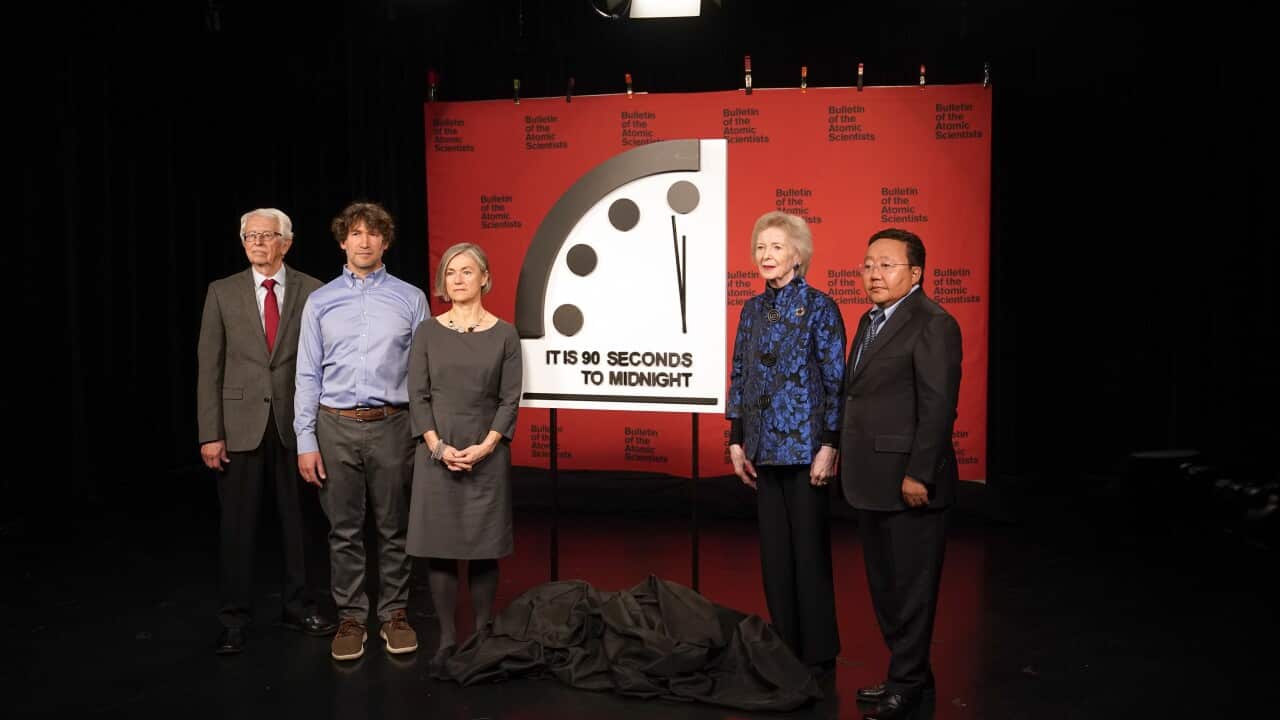 Scientists standing in front of a Doomsday Clock