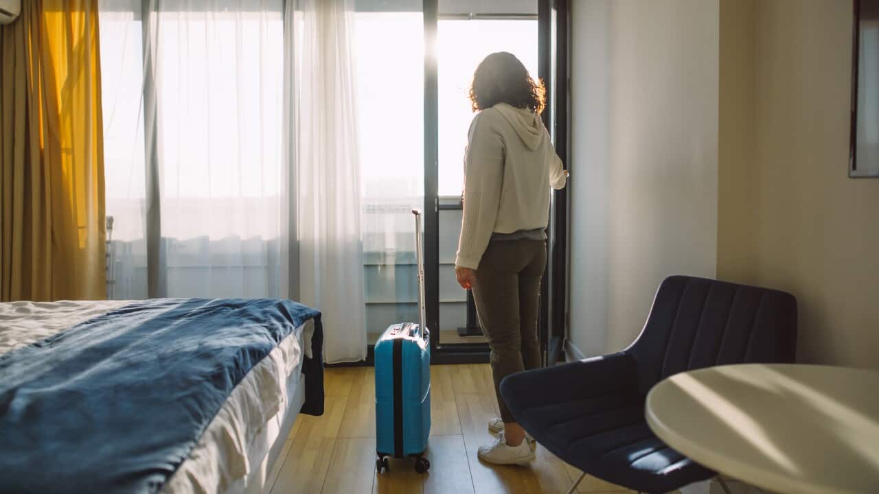 A woman with a blue suitcase on wheels in a room.