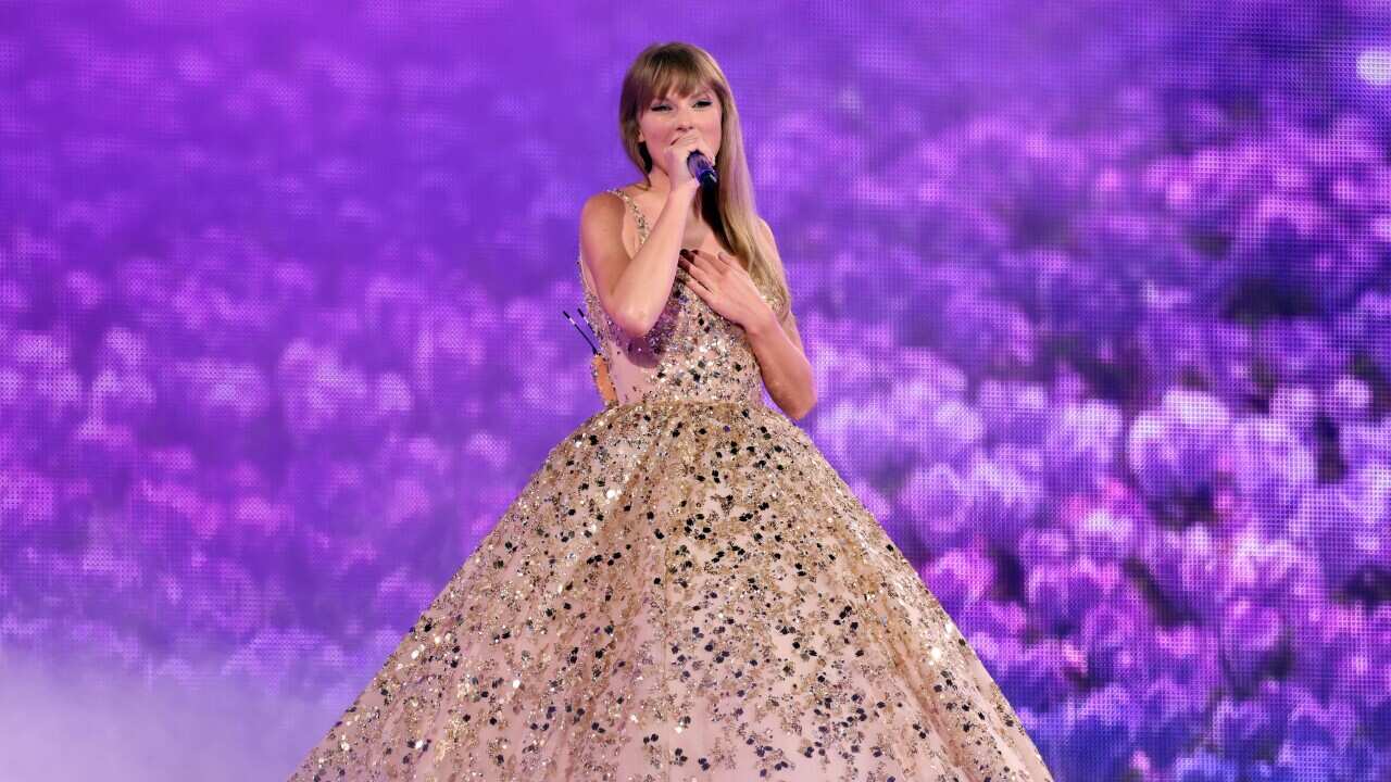 Taylor Swift in a wide-bottomed, sparkly dress singing in front of a purple background.