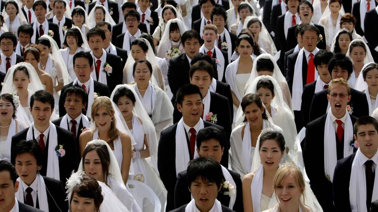 Group of brides and grooms stand side by side at a mass wedding.