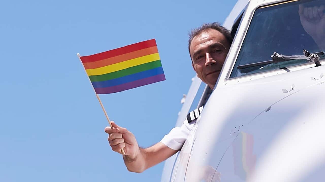 A pilot waving a pride flag out a plane window.