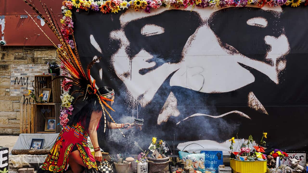An Aztec dancer performs a ceremonial blessing in front of a mural of George Floyd.