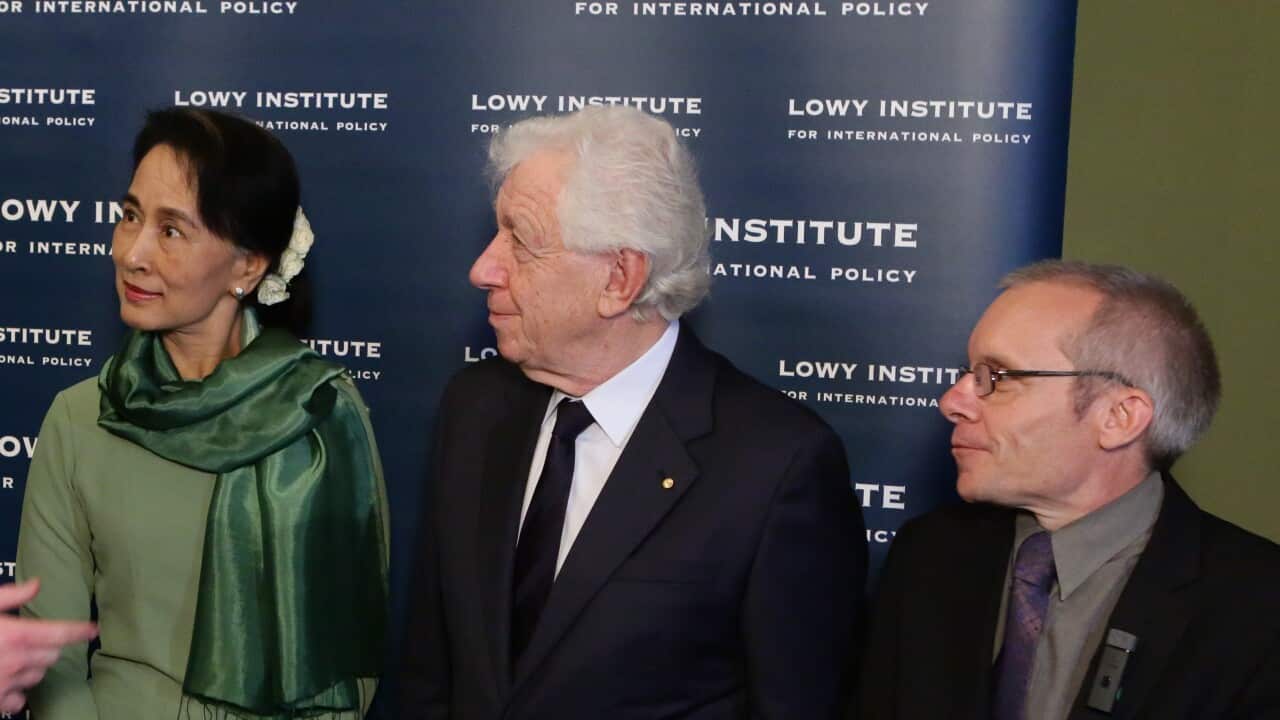 A woman and two men listen to someone speaking.