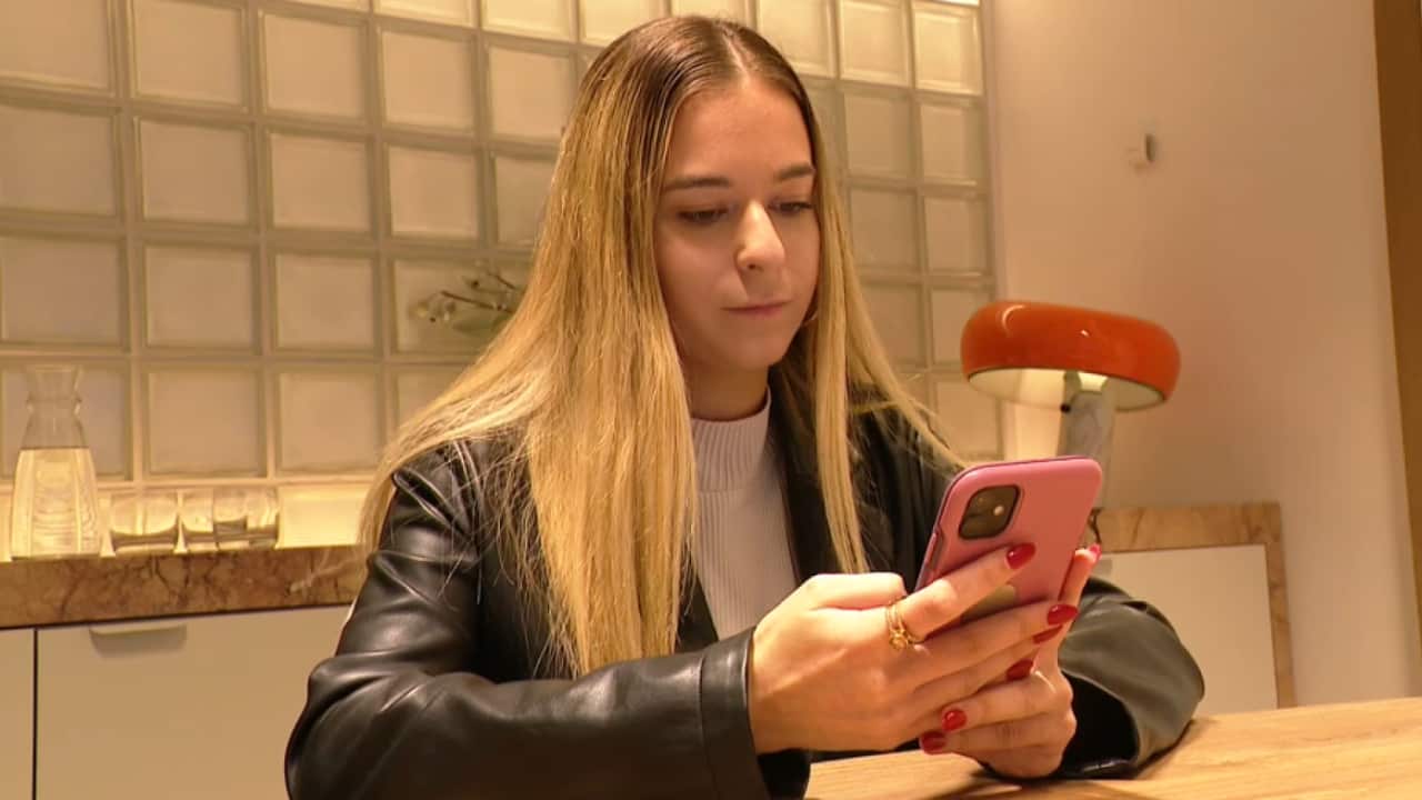 A young woman sits at a table scrolling on her phone.
