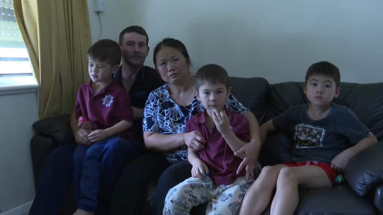A man and woman sit on a couch cuddling their three children