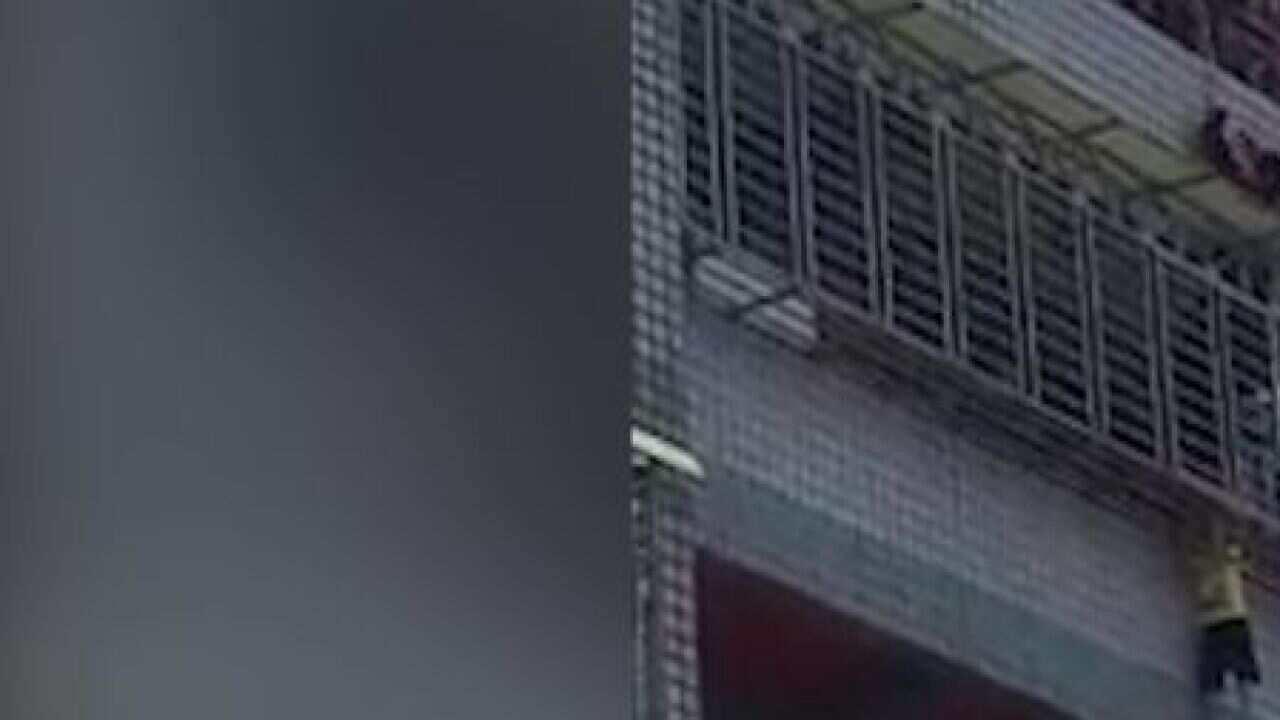 The boy is seen clinging to the security grill enclosure of the balcony on the fifth floor of an apartment building in Taiwan.