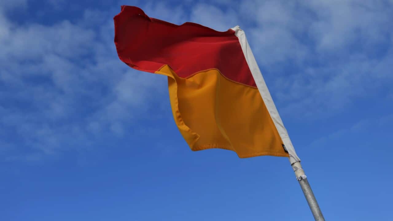 A lifeguard on duty flag stands in the sand