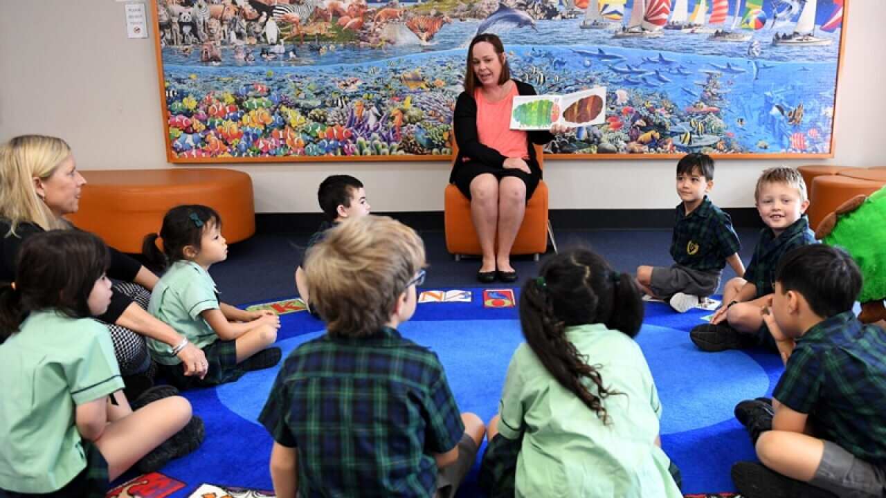A teacher reads a story to young school students