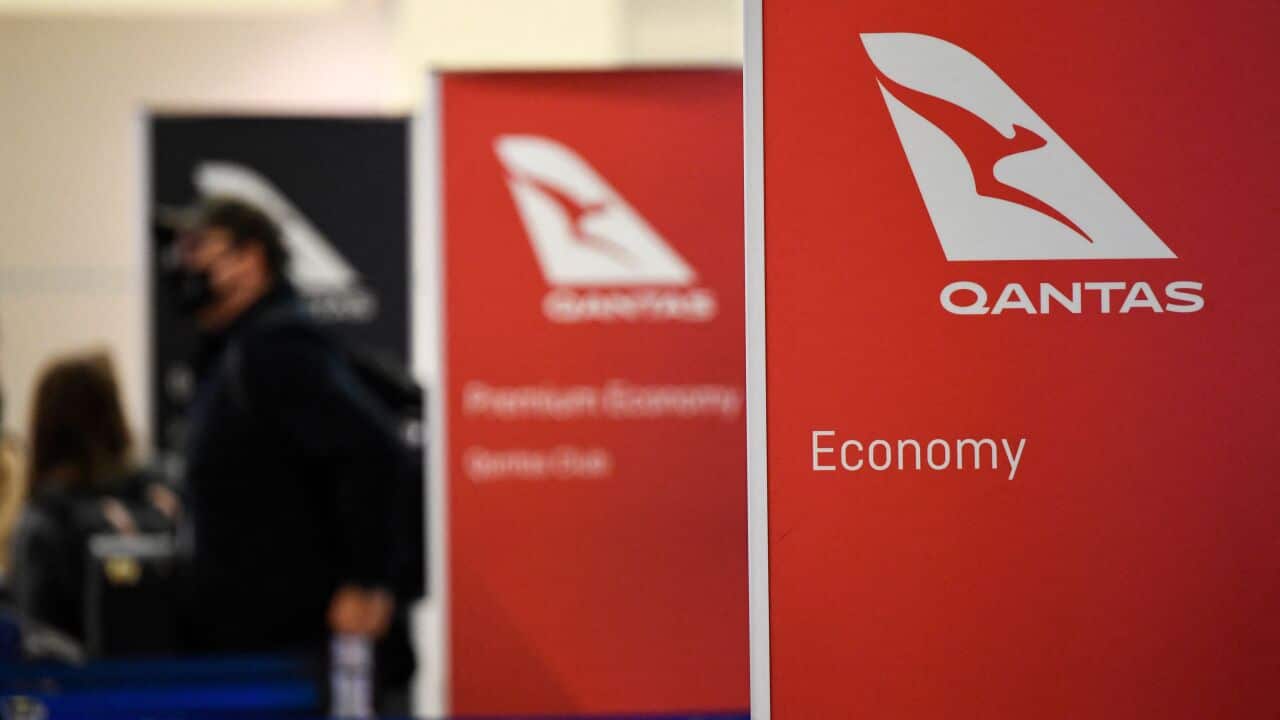 The check in area of an airport with Qantas signs in the foreground and blurred passengers in the background.