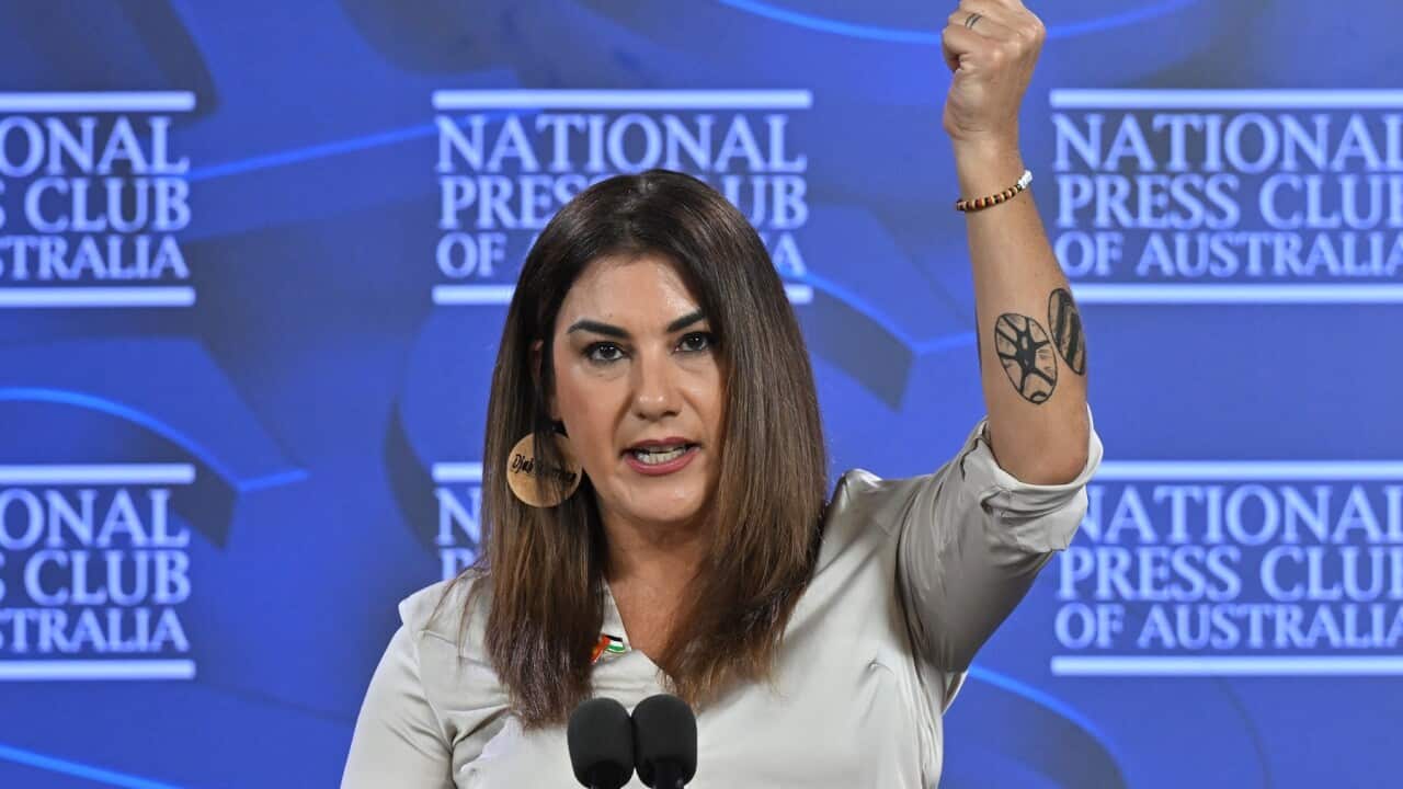 A woman speaks at a lecturn, with one hand raised.