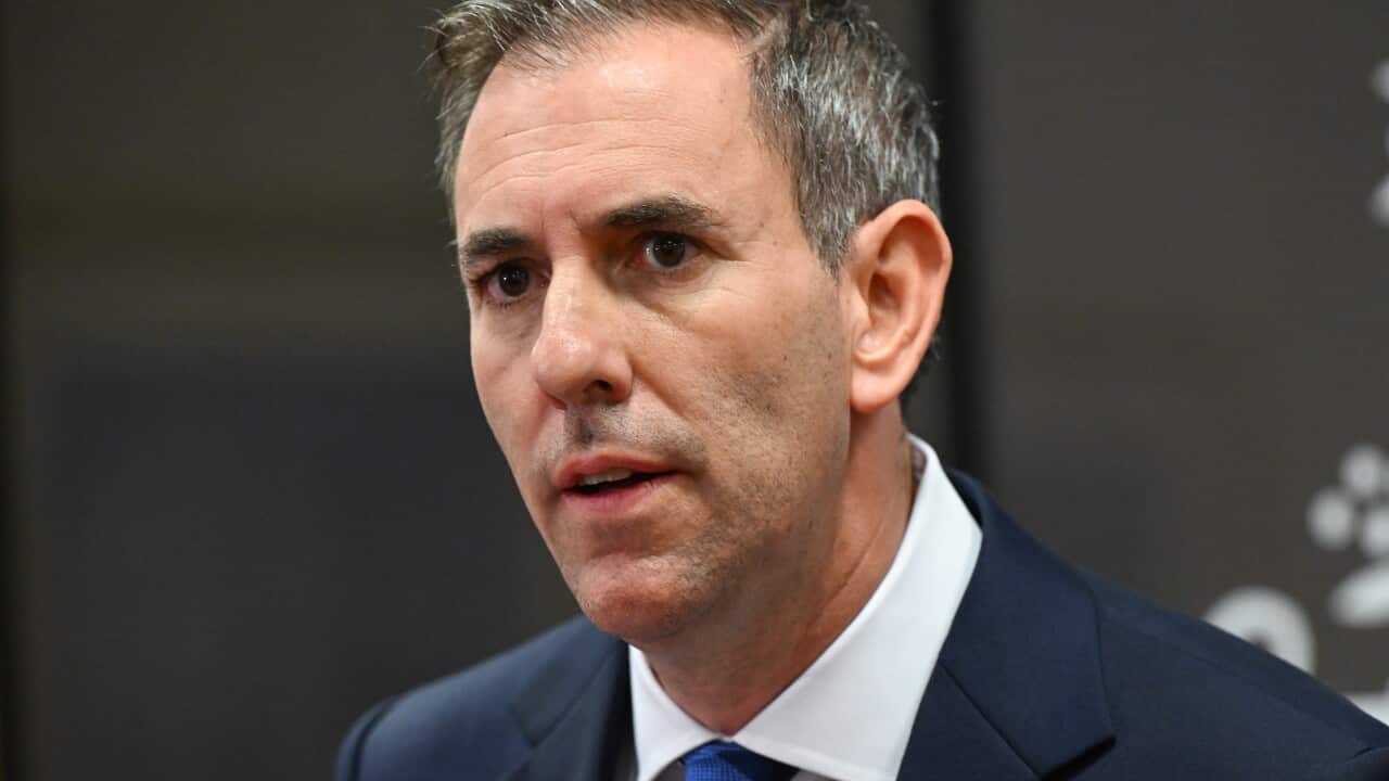 A man in a navy suit and blue tie speaks at a formal press conference with a serious expression.