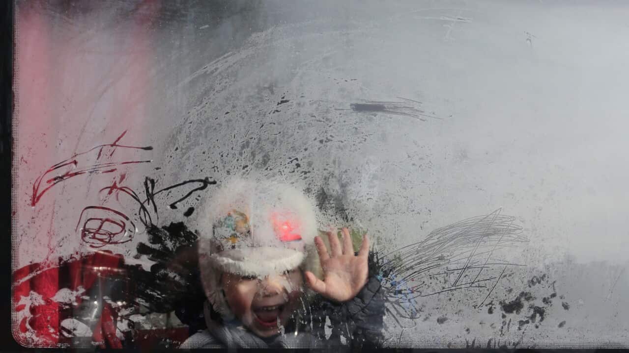 A boy waves as he sits in a bus.