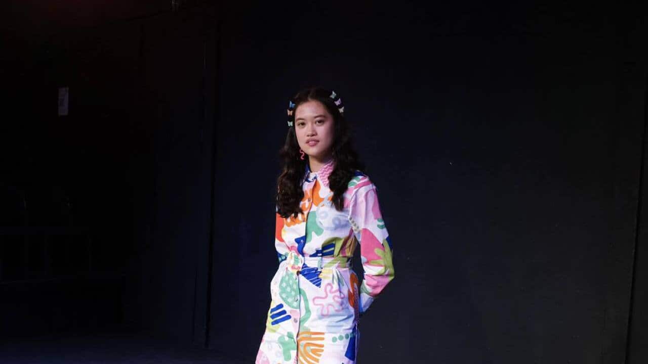 A woman in a dress lit by a spotlight on a stage.