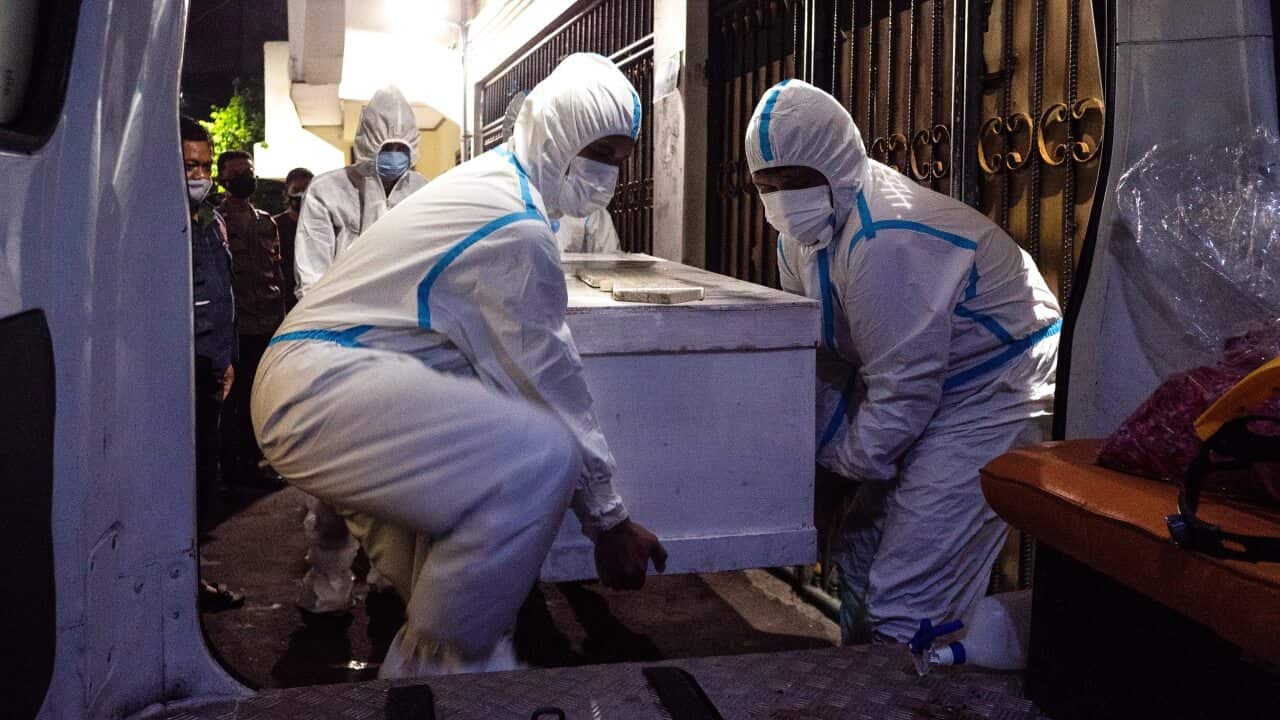 Members of volunteer Polisi Masyarakat (Public Police) carrying the coffin with the body into an ambulance for burial.