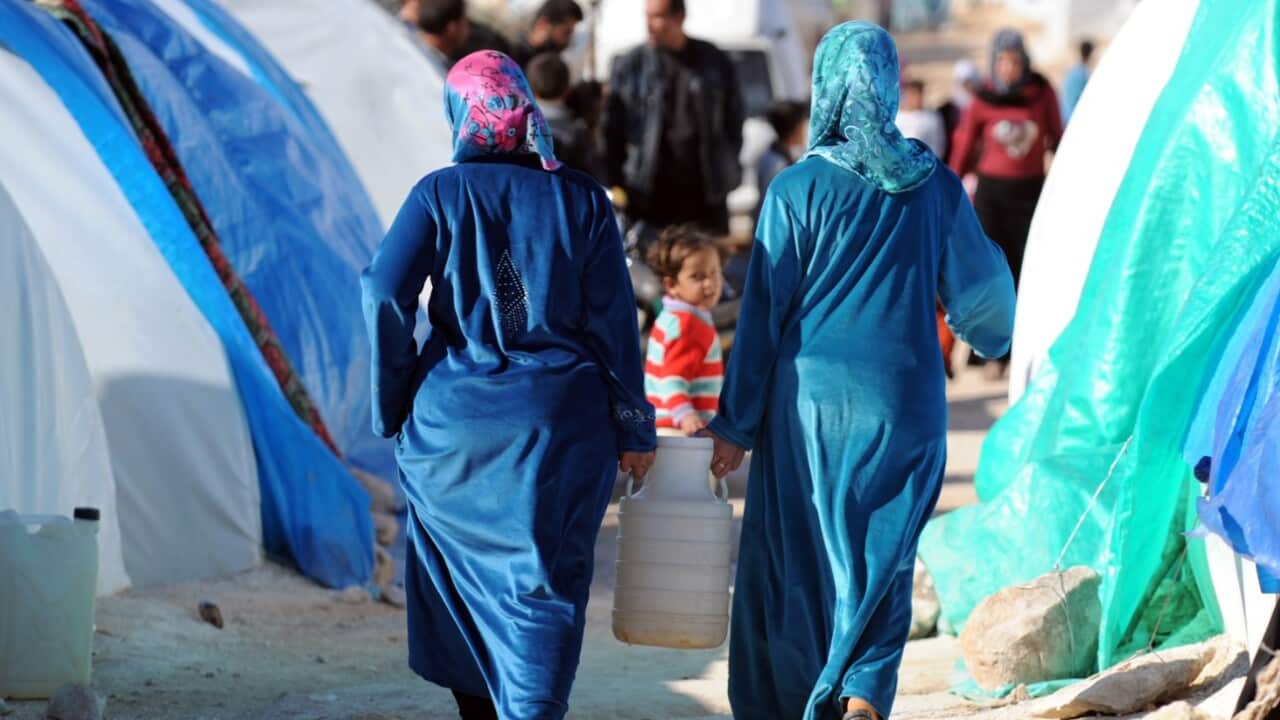 Syrian women carry a water jug back to their makeshift house at the refugee camp of Qah along the Turkish border in the village of Atme