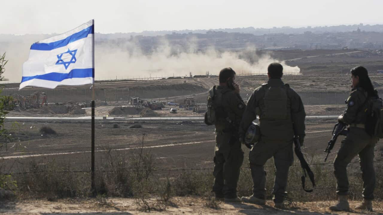 Soldiers standing in a rugged region next to an Israeli flag.
