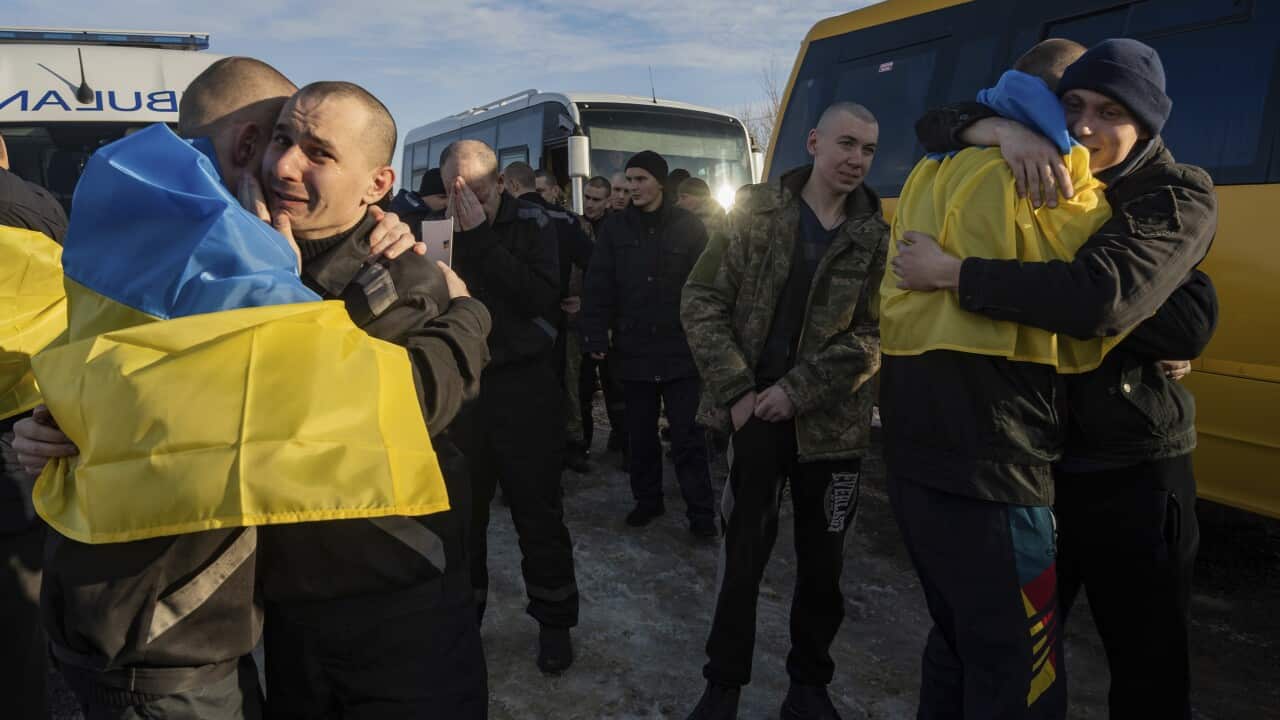 Recently swapped Ukrainian prisoners of war covered in national flags hug each other after a prisoner exchange