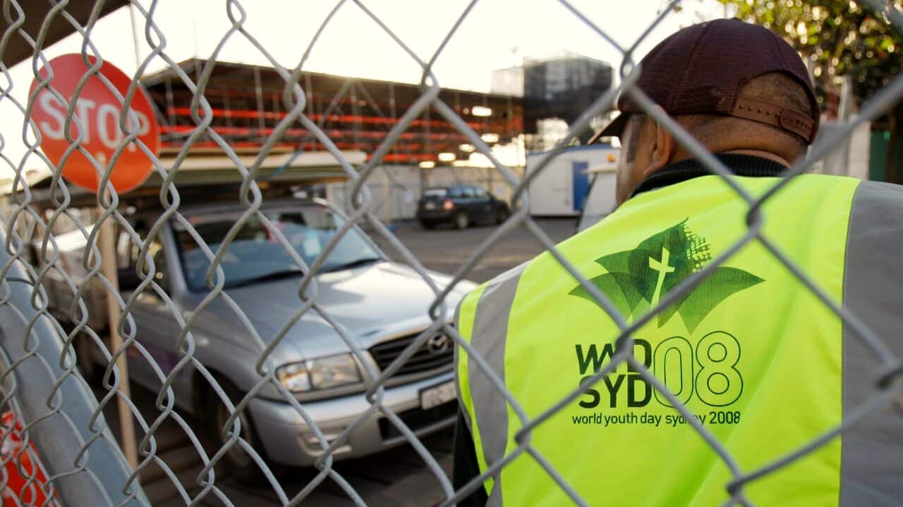 A security guard watches traffic pass through a gate of a wire fence.