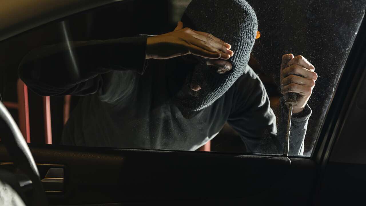 A Burglar is Checking the Interior of the Car on the Street During a Night Hours