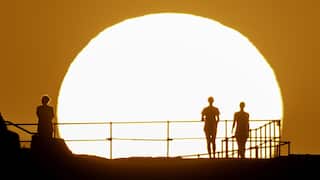 Silhouettes of people against a large, burning white sun in an orange sky.