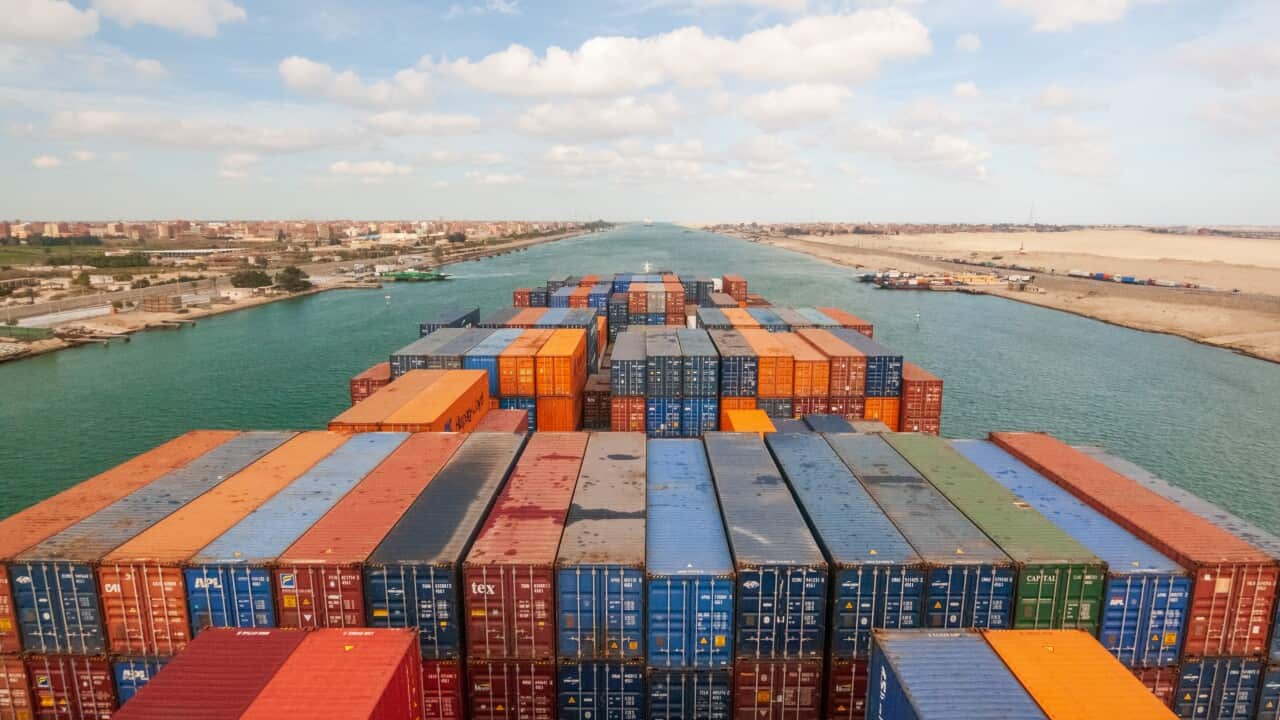 Loaded containers stacked on top of a cargo ship sailing in a canal.