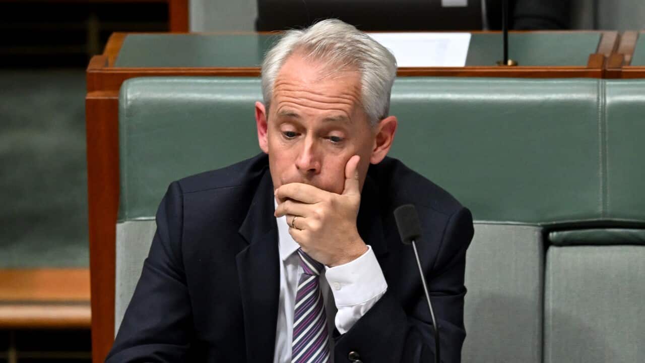 A man sitting in the House of Representatives chamber with his hand to his face