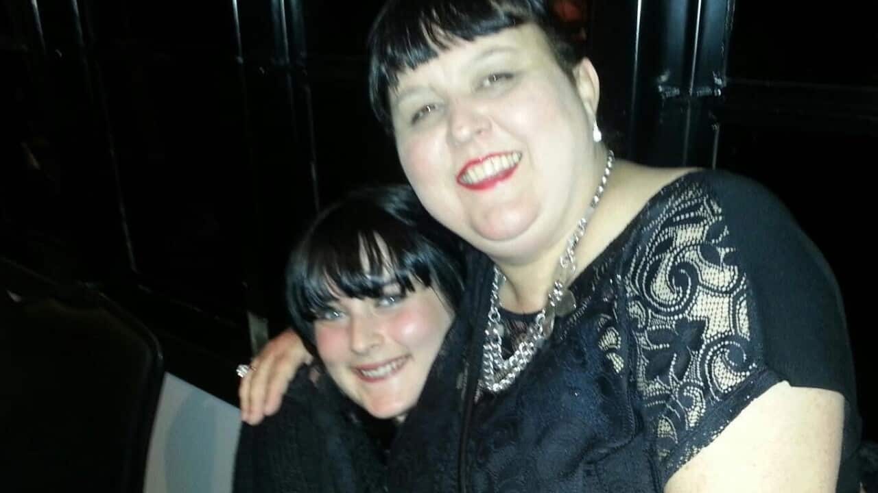 A young woman and middle aged woman both with dark hair and dressed in black hugging each other in a bar