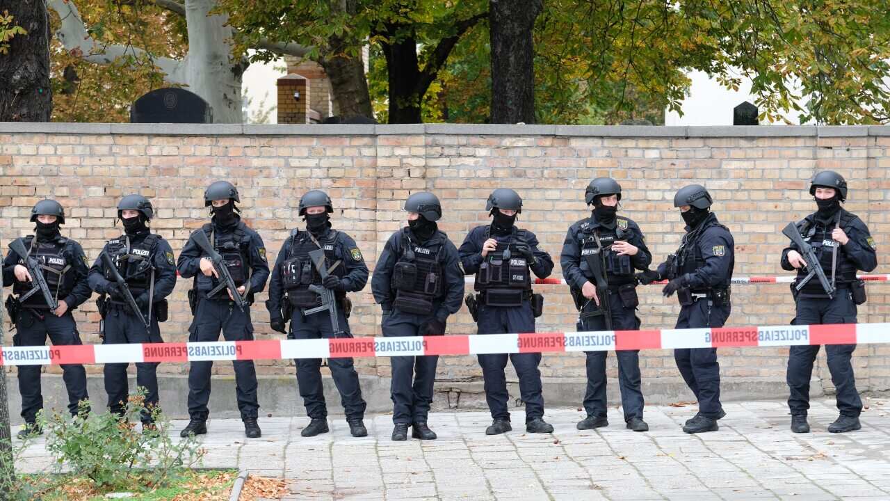 Police officers with helmets secure the area at the Jewish cemetery near the scene, where two people were shot dead in the eastern German city of Halle