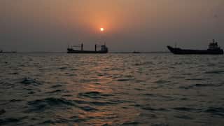 The sun sets over commercial vessels on the sea