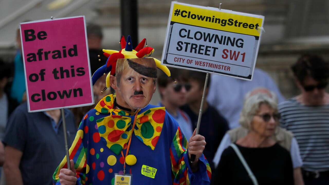 A man dressed as a clown and wearing a Boris Johnson mask protests in front of the Downing Street gate