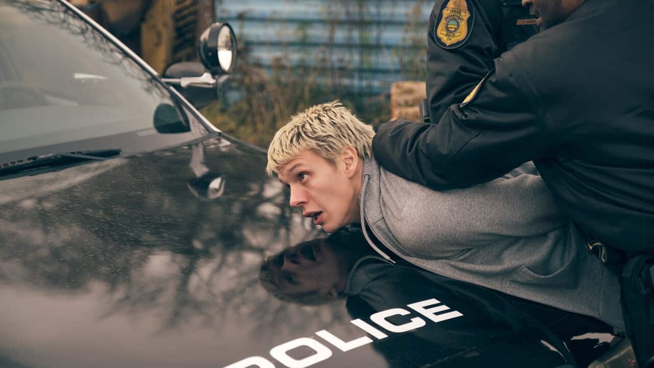 A policeman handcuffs a young man against the bonnet of a police car.jpg