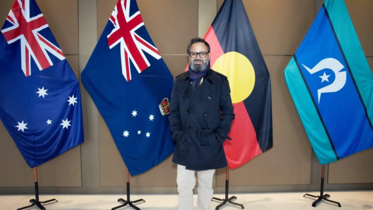 Indian filmmaker Nikkhil Advani posing in front of Australian flags, including the national flag and the Aboriginal flag