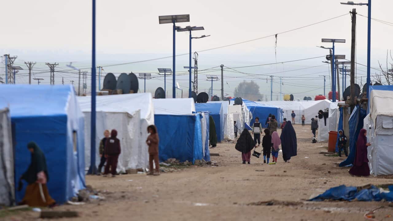 Women and children walk through a camp with large blue and white tents